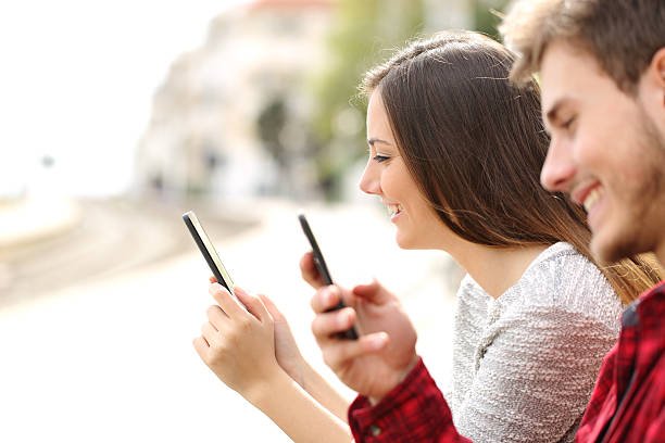 Happy teen couple using smart phones in a train station while they are waiting